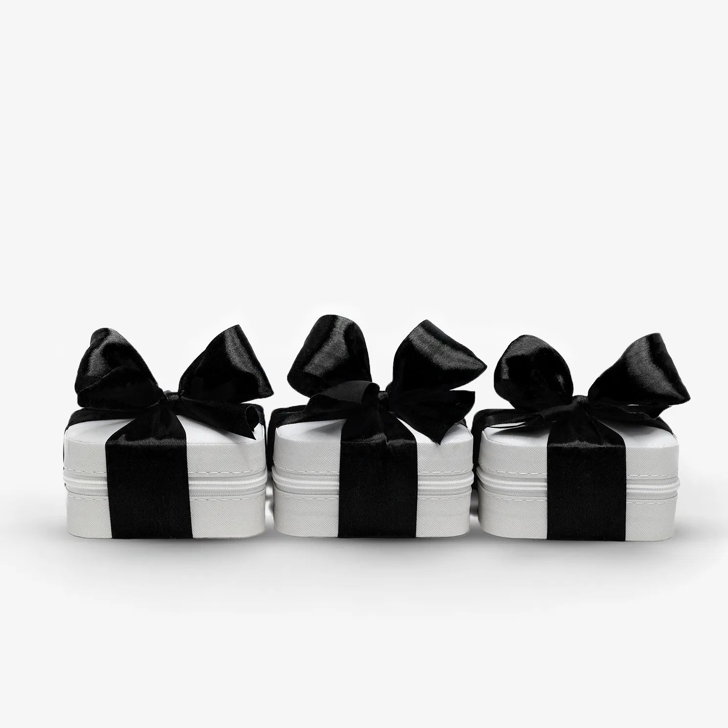 Tre eleganta smyckesaskar i vitt med svarta sidenrosetter – lyxig presentförpackning från Susanna Falken Jewellery.