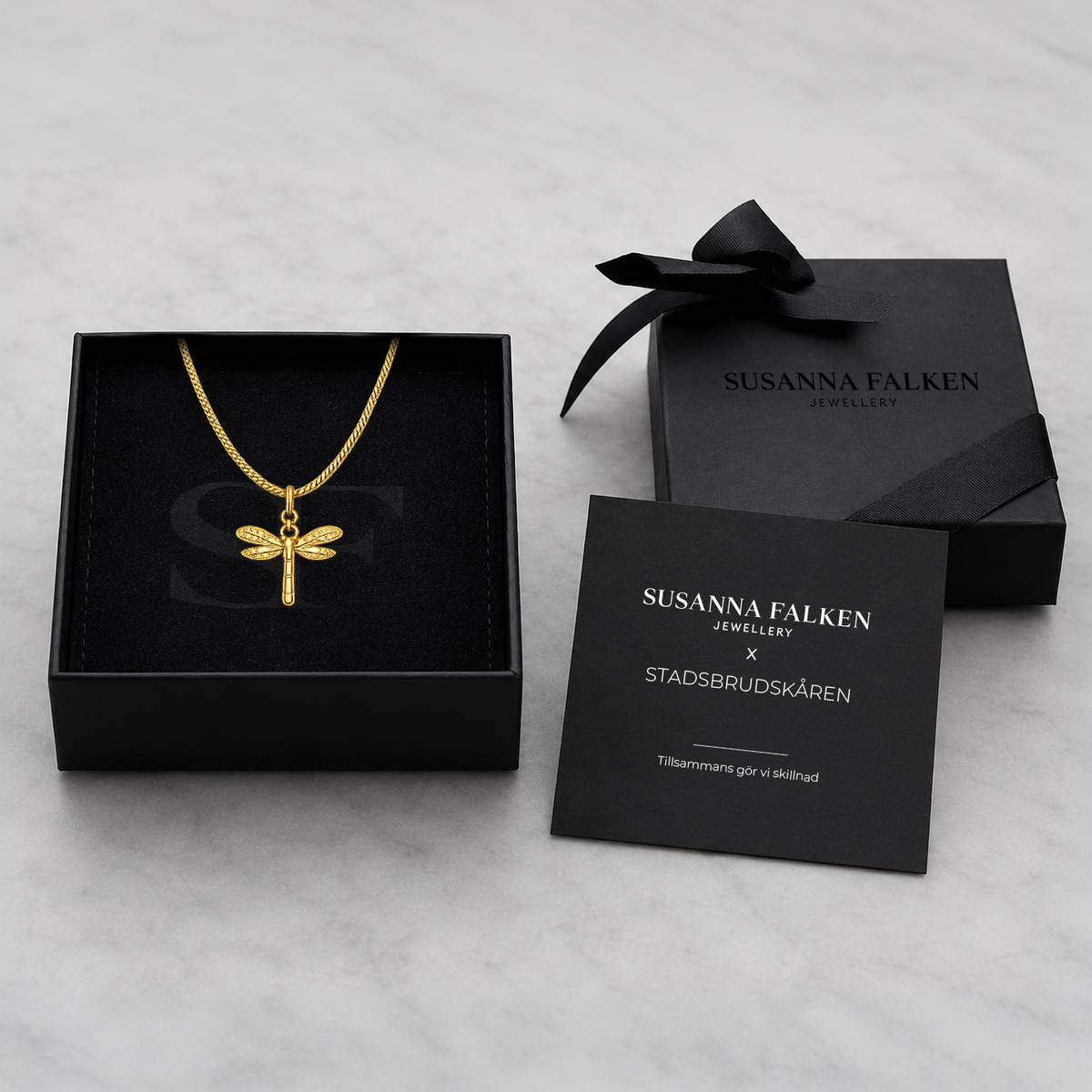 Svart presentask från Susanna Falken Jewellery med Vingkraft Halsband i guld, svart sidenband och tillhörande kort om smyckets betydelse.