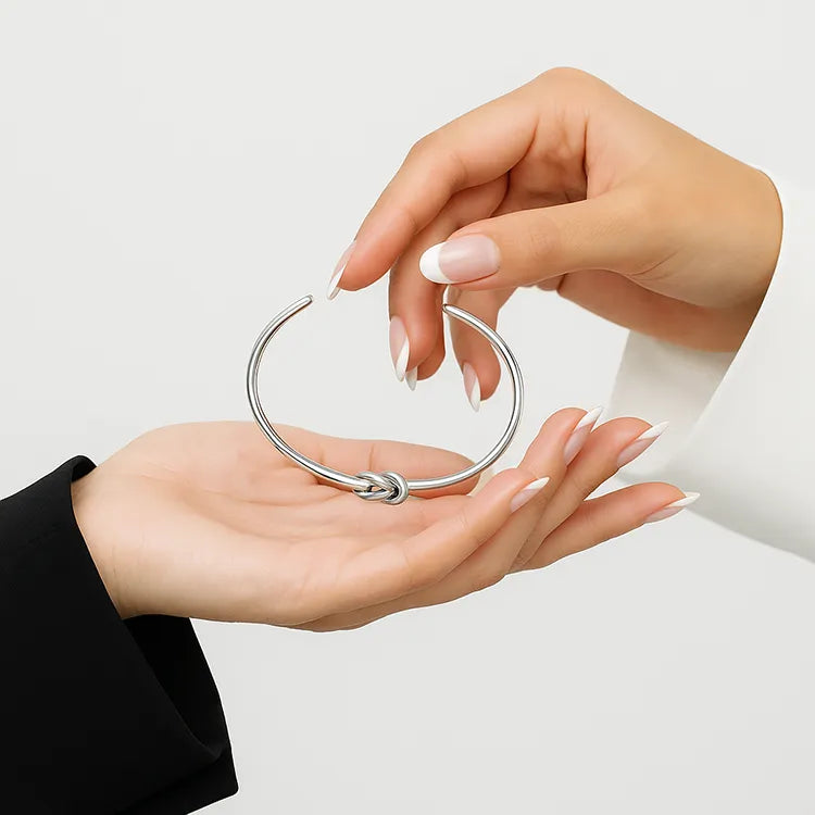 Två kvinnliga händer med fransk manikyr håller ett silverfärgat Friendship-armband från Susanna Falken Jewellery mot en ljus bakgrund. Den ena handen bär svart och den andra vit kavaj – en symbol för vänskap och balans.